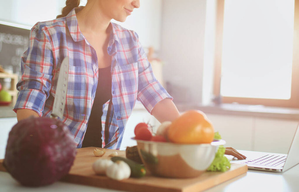 Young woman cutting vegetables in kitchen near desk. - Foto, afbeelding