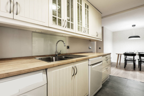 White kitchen cabinets with wooden countertop and dining table in the background - Fotó, kép