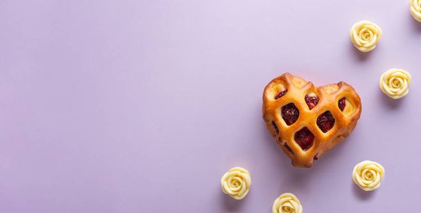 Valentýnský prapor. Srdečně tvarovaná houska s mřížkovou kůrkou a jahodovou marmeládou na purpurovém pozadí s bílými čokoládovými růžemi. Flat lay, copy space for text - Fotografie, Obrázek