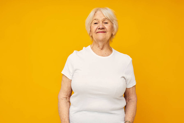 elderly woman in casual t-shirt gestures with his hands yellow background - Foto, Imagen