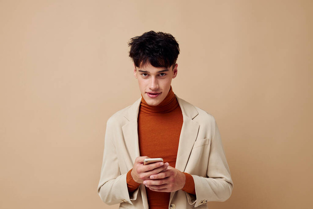 A young man posing with a phone in his hands in a jacket elegant style model studio - Foto, imagen
