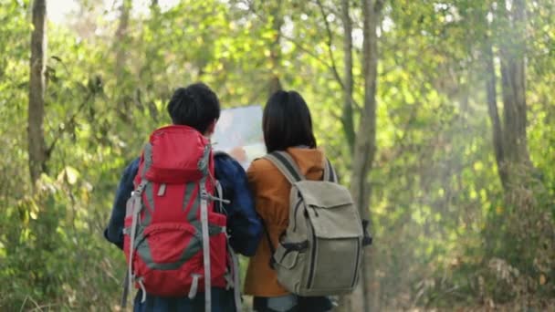 Νεαρό ζευγάρι Ασιάτες τουρίστες που περπατούν στο δάσος για ηλιόλουστο όμορφο καλοκαίρι και τον έλεγχο του χάρτη χαρτί και να απολαύσετε τον τρόπο ζωής των διακοπών. - Πλάνα, βίντεο