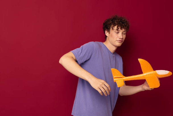 kinky guy with a toy plane in a purple t-shirt red background unaltered - Fotoğraf, Görsel