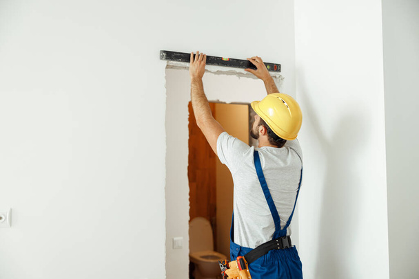 Professional handyman, male worker in uniform using spirit level while taking measurements indoors - Photo, Image