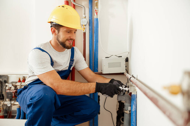 Cheerful male worker, plumber checking pipes while installing heating system in apartment - Foto, Bild