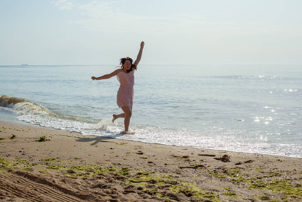 chica en vestido rosa corre en las olas del mar al mediodía.  - Foto, Imagen