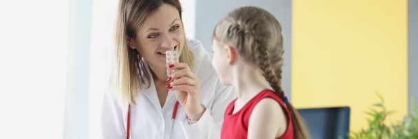 Woman doctor showing little girl blister with medication in clinic - 写真・画像