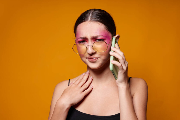 Young beautiful woman with a phone in hand bright makeup posing fashion emotions yellow background unaltered - Foto, Bild