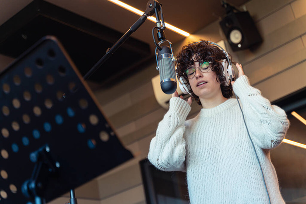 Egy fiatal, göndör hajú, szemüveges nő, aki egy igazi stúdióban vesz fel egy dalt.  - Fotó, kép