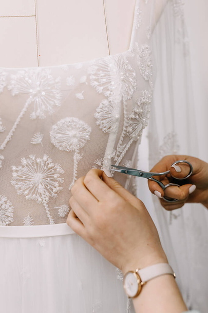 Primer plano del sastre fabricación de un vestido de novia, el corte de un hilo. - Foto, Imagen