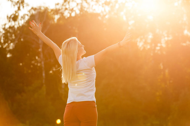 Atrakcyjna młoda kobieta cieszy się czasem spędzonym na zewnątrz w parku z zachodem słońca w tle. - Zdjęcie, obraz