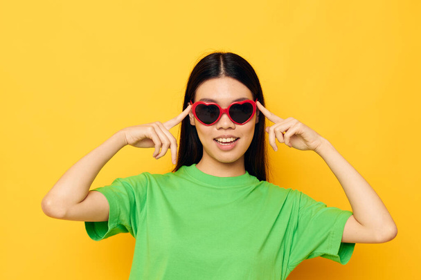 Charming young Asian woman in dark glasses in a green t-shirt posing modern yellow background unaltered - Фото, зображення