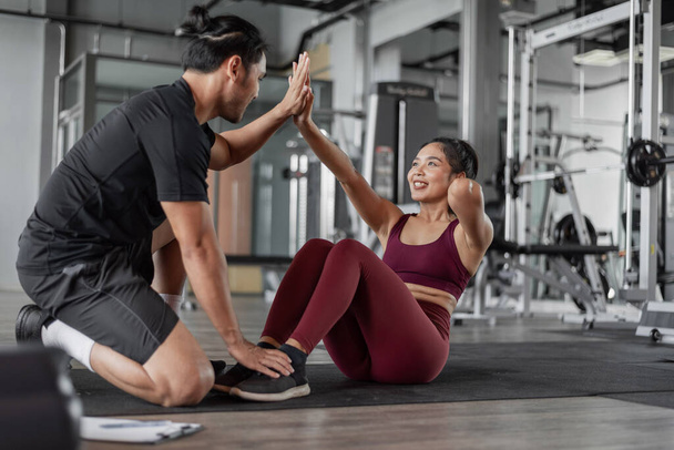 Asiatische Frauen trainieren mit Personal Trainer im Fitnessstudio. Gesunde Frau beim Bauchmuskeltraining mit Personal Coach. - Foto, Bild