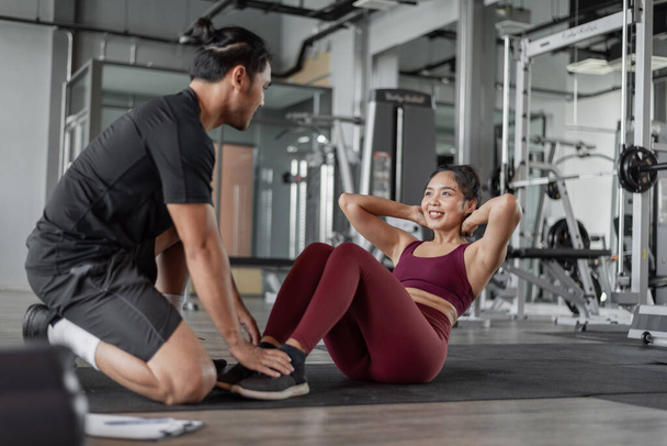 Aziatische vrouw oefening met personal trainer in de sportschool. Gezonde vrouw doet buikspieroefeningen in fitness met personal coach. - Foto, afbeelding