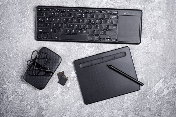 Top view of designer work place with graphics tablet, keyboard and portable hard drive on grey concrete background - Foto, Imagen