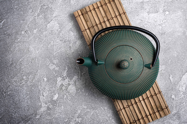 Traditional green asian cast iron kettle on bamboo mat and grey concrete background - Photo, image