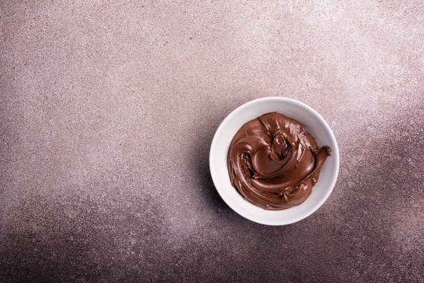 Delicious chocolate cream or brown nut butter, paste as ingredient for tasty homemade dessert on concrete background with copy space - 写真・画像