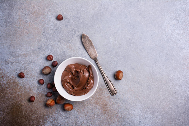Delicious chocolate cream or brown nut butter, paste and whole hazelnut as ingredient for tasty homemade dessert on concrete background - 写真・画像