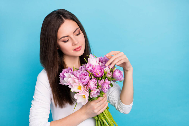 Portrait of attractive cute sweet girl holding flowers touching petals isolated over brigth blue color background - 写真・画像