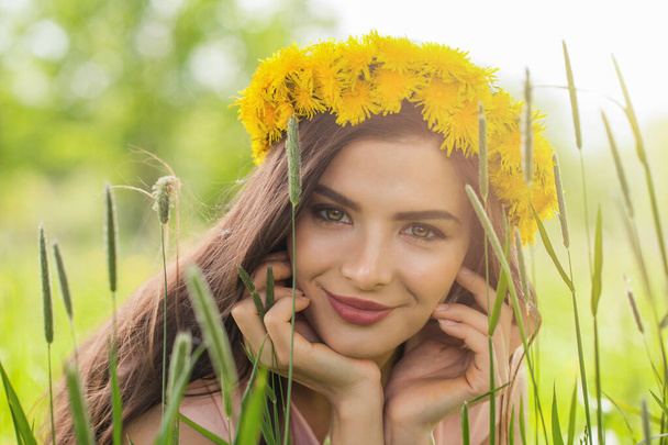 Young spring fashion woman wearing yellow dandelion wreath in spring field. Springtime - Фото, изображение