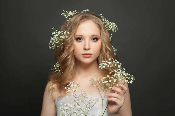Портрет молодої жінки. Симпатична жіноча модель з натуральним макіяжем і здоровим кучерявим волоссям, що тримає квіти
 - Фото, зображення