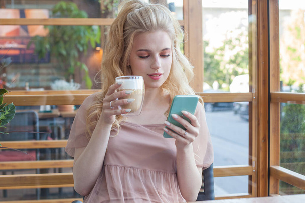 魅力的なブロンド女性タイピングテキストメッセージ上のスマートフォンでA caf é - 写真・画像