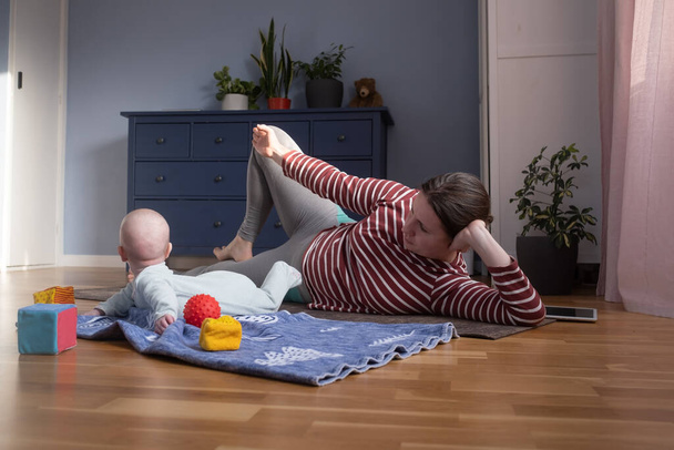 Λευκή μητέρα με μωρό κάνει γιόγκα στο σπίτι για να είναι ισχυρή και υγιής, - Φωτογραφία, εικόνα