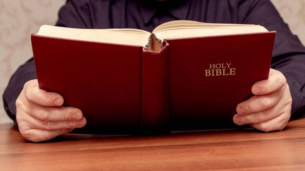 Een man houdt een open bijbel in zijn handen. De Bijbel lezen en bestuderen - Foto, afbeelding