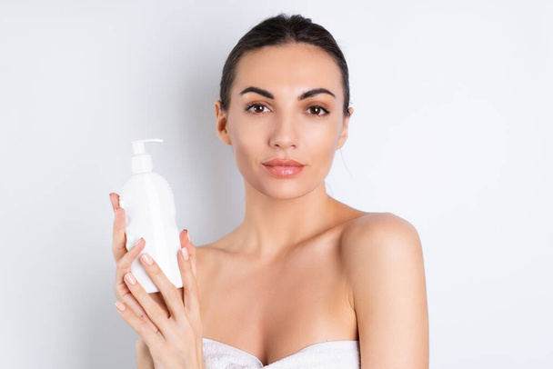 Fechar retrato de beleza de uma mulher de topless com pele perfeita e maquiagem natural segurando garrafa de xampu, loção corporal, em um fundo branco - Foto, Imagem