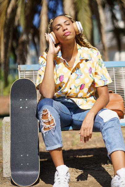 Afrikanisches Mädchen mit Skateboard entspannt sich nach dem Skateboardfahren und hört Musik - Foto, Bild
