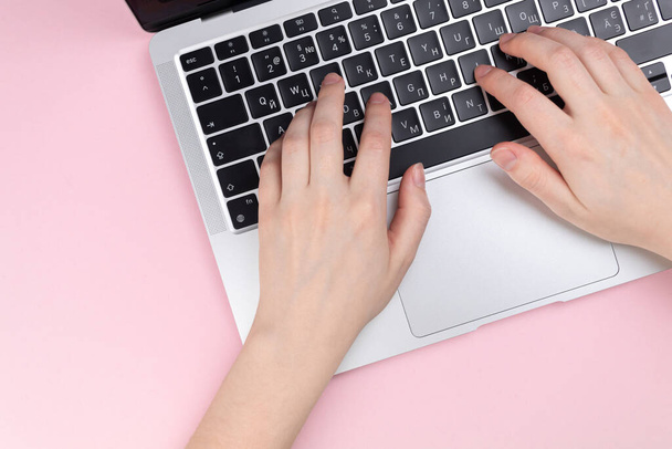 Mani femminili e tastiera del computer portatile su uno sfondo rosa. Concetto di spazio di lavoro, lavoro al computer, freelance e design. Layout piatto, vista dall'alto e spazio di copia - Foto, immagini
