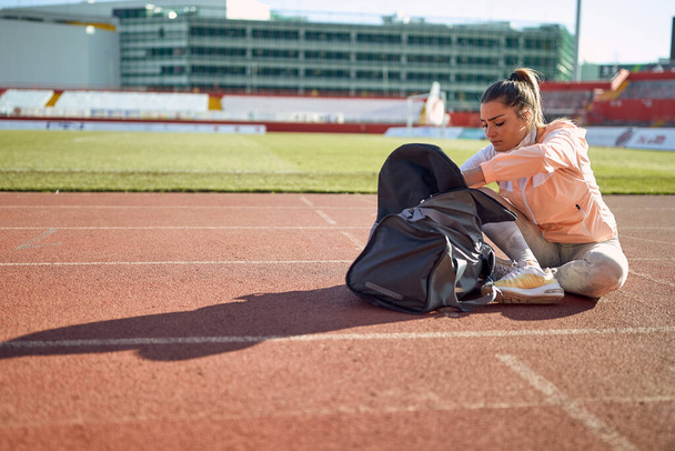 Una giovane donna è seduta in pista e si prepara per un allenamento in una bella giornata allo stadio. Sport, atletica, atleti - Foto, immagini