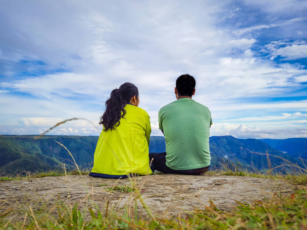 Genç çift, sabah vakti açık mavi gökyüzüyle dağın tepesinde oturuyor. - Fotoğraf, Görsel