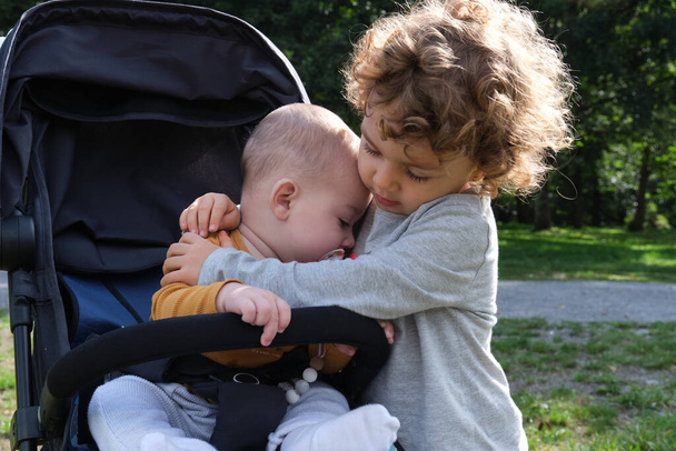 boldog kishúga öleli kisöccse ül a baba babakocsi egy természetes parkban - Fotó, kép