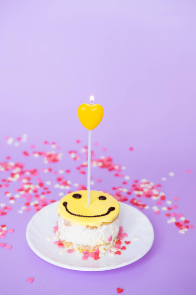yellow cake smiley with a candle in the form of a heart on a purple background. Valentine's day and birthday concept - Foto, afbeelding