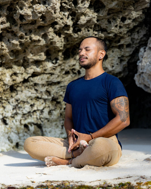 Medytacja i joga na plaży. Azjata siedzący na piasku w pozycji Lotusa. Padmasana. Ręce w mudrze blokady Jowisza. Zamknięte oczy. Odwrót jogi. Zdrowy styl życia. Plaża Thomas, Bali, Indonezja - Zdjęcie, obraz