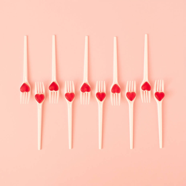 Creative arrangement made of white forks with red candy hearts on pastel pink background. Minimal Valentines day or wedding layout. Flat lay. - Fotografie, Obrázek
