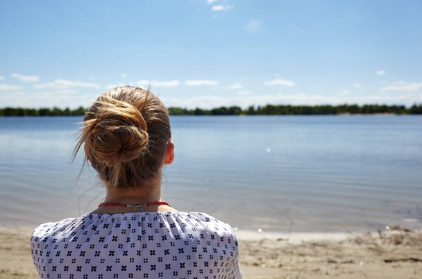 Girl sitting on the coast and looking into the distance. Young woman resting at water. Enjoy life, having fun, leisure, relaxation, lifestyle concept. Rear view - Foto, Imagem