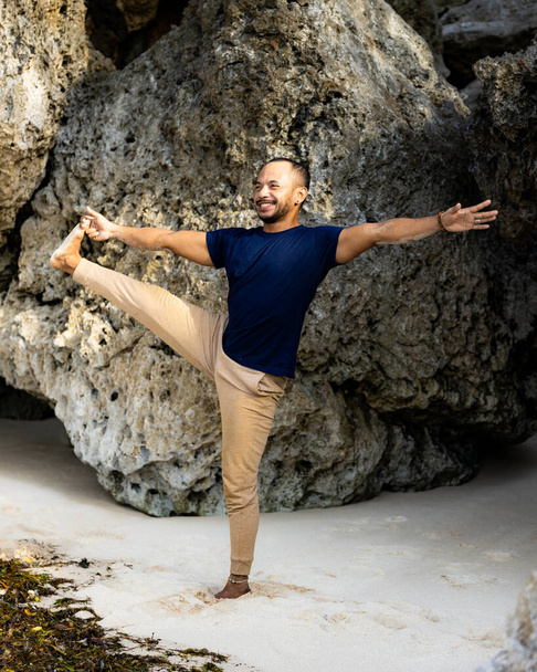 Joven asiático practicando Utthita Hasta Padangusthasana, Standing Big Toe Hold. Haz ejercicio en la playa. Cuerpo fuerte. Balance asana. Retiro de yoga. Estilo de vida saludable. Playa de Thomas, Bali, Indonesia - Foto, imagen
