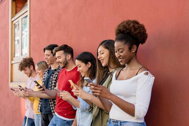 Młoda wielorasowa grupa przyjaciół korzystająca z mobilnego smartfona outdoor - pokolenie Millennial bawiące się nowymi trendami aplikacje społecznościowe - Technologia młodzieżowa ludzie uzależnieni - Zdjęcie, obraz