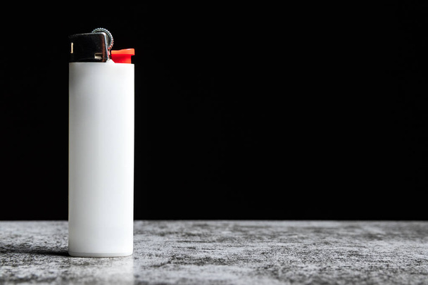 Белая зажигалка на сером столе на черном фоне с копировальным пространством. - Фото, изображение