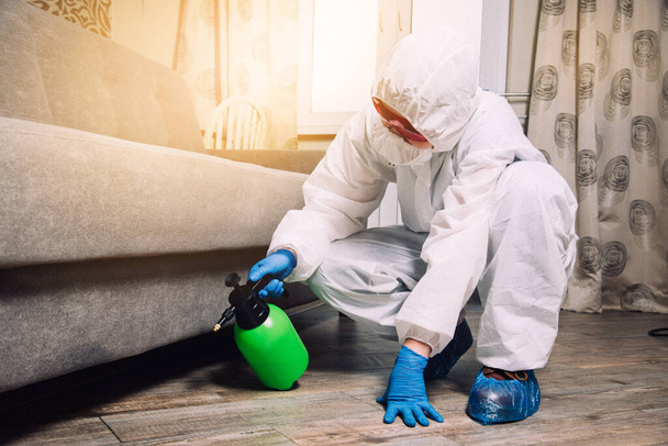 An exterminator in work clothes sprays pesticides with a spray gun. Fight against insects in apartments and houses. Disinsection of the premises. - Zdjęcie, obraz