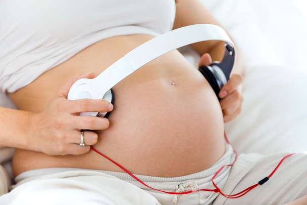 Pregnant woman putting headphones on her belly  - Fotó, kép