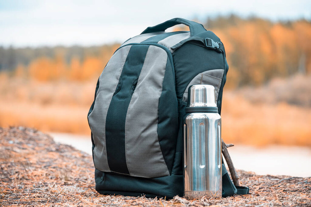 Hiking backpack with thermos for tea on the river bank - 写真・画像