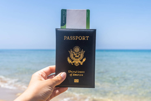 Woman holding american passport with boarding pass in a cover opposite sea wave beach. Concept of summer travel, tourism, holiday. - Zdjęcie, obraz