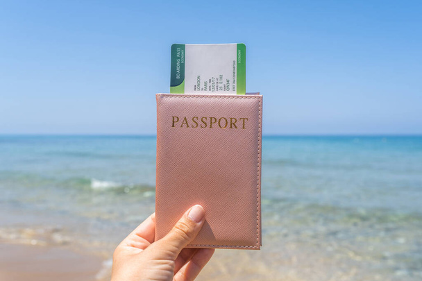 Woman holding passport with boarding pass in a cover opposite sea wave beach. Concept of summer travel, tourism, holiday. - Foto, imagen