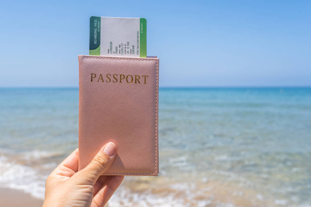 Woman holding passport with boarding pass in a cover opposite sea wave beach. Concept of summer travel, tourism, holiday. - Zdjęcie, obraz