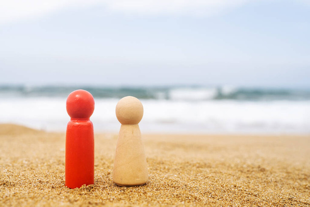 Wooden two figures of different color of people red, dark and white  on the sand of beach with sea view. Concept of happy couple on holiday. International, different race.  - Foto, Bild