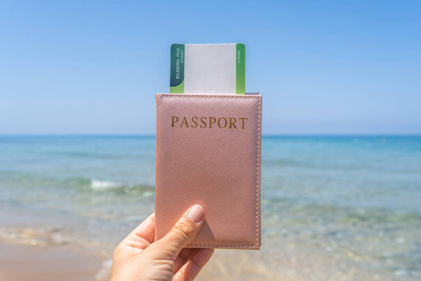 Woman holding passport with boarding pass in a cover opposite sea wave beach. Concept of summer travel, tourism, holiday. - Zdjęcie, obraz