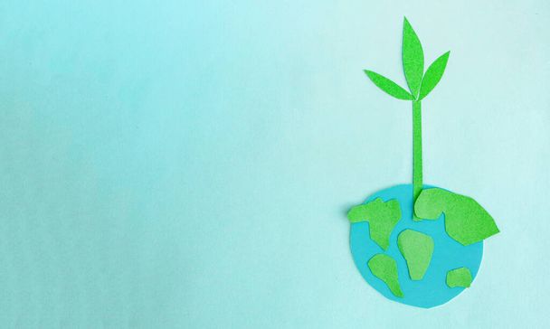 Cute children's paper applique -a model of the Earth and a young sprout on a blue background. Creative concept Earth Day, Earth Hour, copy space for text. - Photo, Image